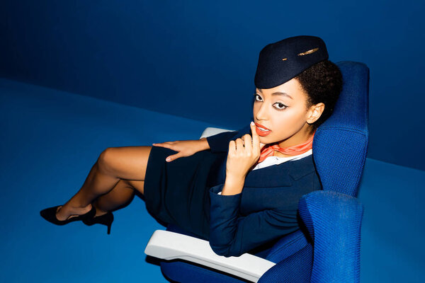 high angle view of african american flight attendant sitting on seat on blue background 