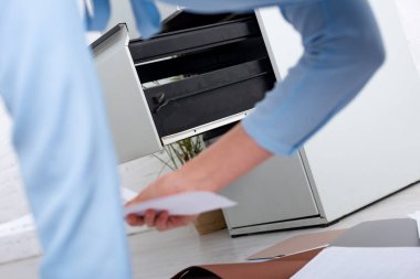 Selective focus of open cabinet driver and businesswoman with documents on floor in office clipart