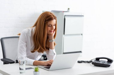 Smiling businesswoman using laptop near phone on table