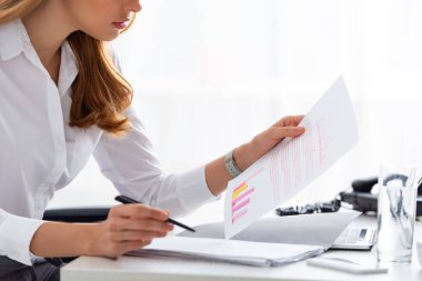 Cropped view of businesswoman working with documents and charts at table