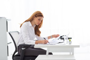Side view of businesswoman working with papers and charts at office table 