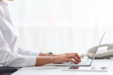 Cropped view of businesswoman using laptop near gadgets on table
