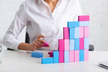 Cropped view of businesswoman stacking building blocks at working table 