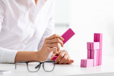 Selective focus of businesswoman stacking marketing pyramid from pink blocks wood game on table clipart