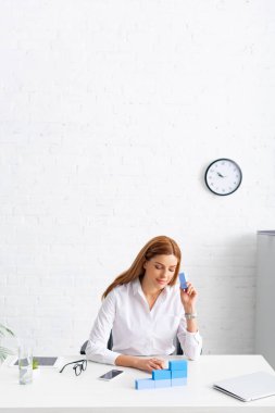Businesswoman making marketing pyramid from blue building blocks near gadgets on table