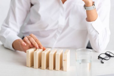 Selective focus of businesswoman stacking wooden building blocks near eyeglasses and glass of water on table isolated on grey  clipart