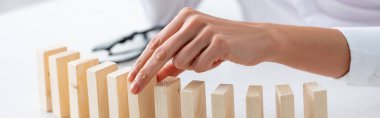 Cropped view of businesswoman holding wooden building block at table isolated on grey, panoramic shot 