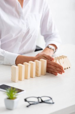 Selective focus of businesswoman folding falling building blocks near smartphone and eyeglasses on table on grey background