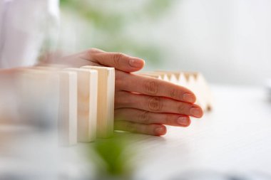 Selective focus of businesswoman folding falling building blocks on table on grey background