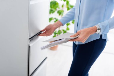 Cropped view of businesswoman holding folder with dossier and opening cabinet driver 