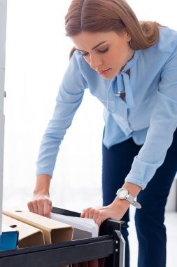 Attractive businesswoman searching folder with dossier from cabinet driver on white background