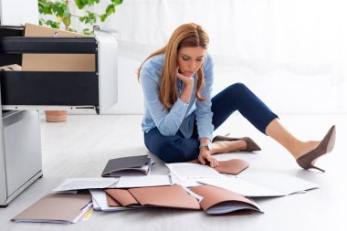Attractive businesswoman looking at contract and documents near open cabinet driver on floor
