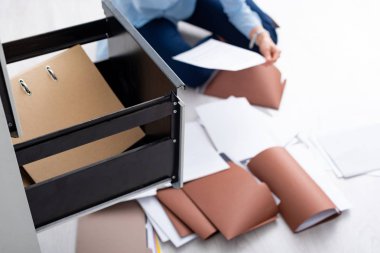 Selective focus of businesswoman with documents near open cabinet driver sitting on floor clipart