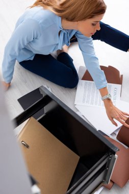 Selective focus of businesswoman with dossier and contract sitting on floor near open cabinet driver 