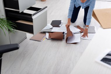 Cropped view of businesswoman searching dossier near contract on floor in office