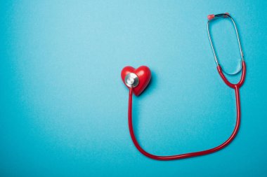 Mavi arka planda kırmızı steteskopla bağlantılı dekoratif kalbin üst görünümü, dünya sağlık günü konsepti