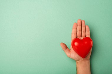Yeşil arka planda insan eliyle dekoratif kırmızı kalbin üst görüntüsü, dünya sağlık günü konsepti