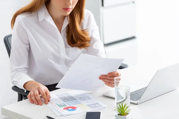 Cropped View Businesswoman Holding Paper Graphs Smartphone Laptop Table — Stock Photo, Image