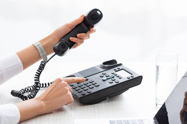 Cropped view of businesswoman using phone near glass of water and laptop on table