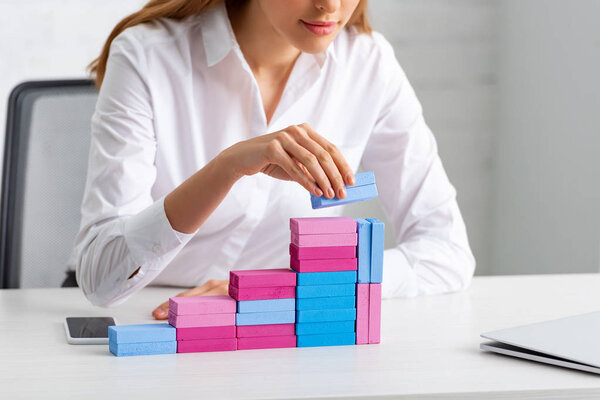 Cropped view of businesswoman stacking marketing pyramid from building blocks on table in office