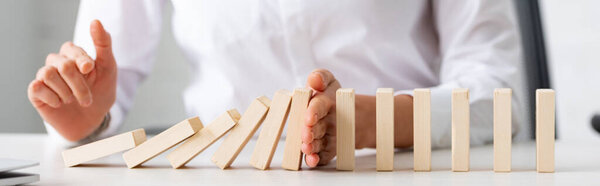 Panoramic shot of businesswoman holding falling building blocks on table