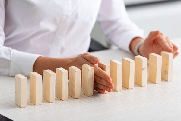 Cropped view of businesswoman holding wooden building blocks on table