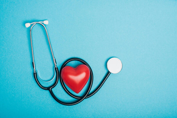 Вид сверху декоративного красного сердца со стетоскопом на синем фоне, концепция Всемирного дня здоровья
