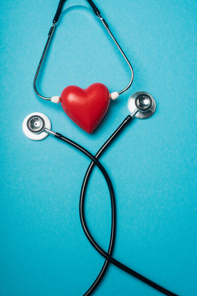 Top view of decorative red heart with black stethoscope on blue background, world health day concept