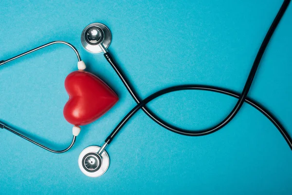 青の背景に装飾的な赤いハートと黒の聴診器のトップビュー 世界健康デーの概念 — ストック写真