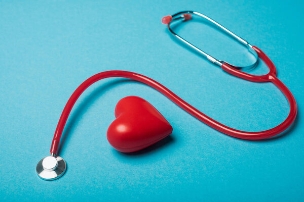Decorative heart next to red stethoscope on blue background, world health day concept
