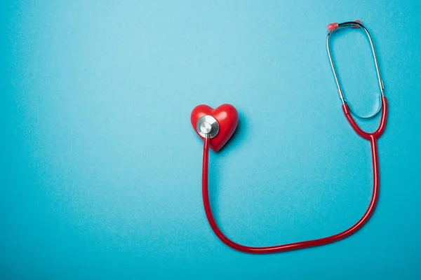 青い背景に赤い聴診器で接続された装飾的な心のトップビュー 世界健康デーの概念 — ストック写真