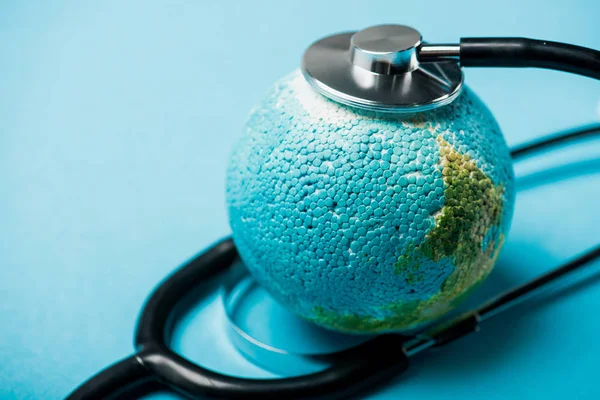 蓝色背景下与地球相连的黑色听诊器的选择性聚焦 世界卫生日的概念 — 图库照片