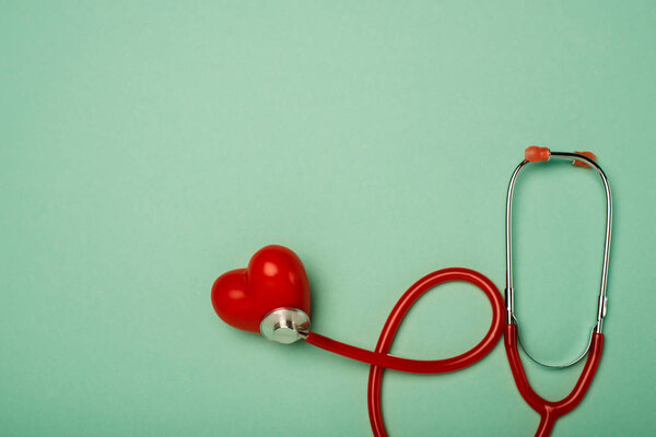 Top view of stethoscope connected with decorative red heart on green background, world health day concept