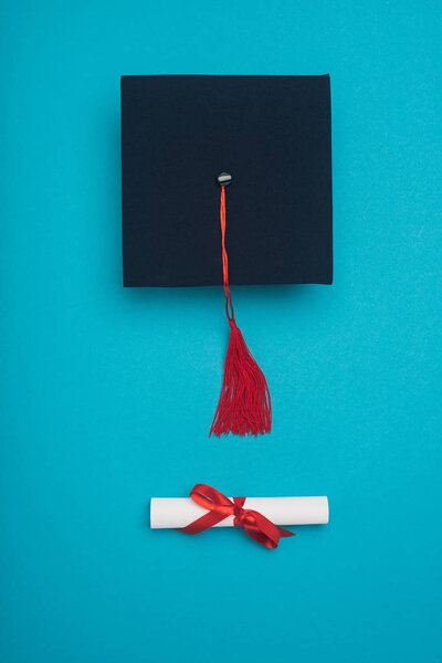 Top view of graduation cap with red tassel and diploma on blue background