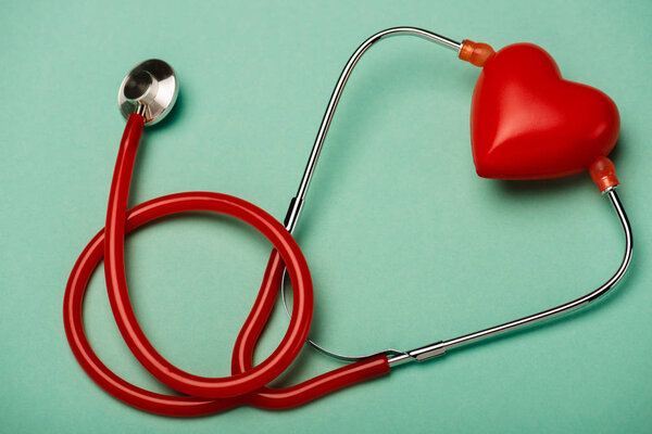 Red stethoscope and decorative heart on green background, world health day concept