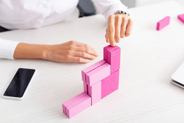 Cropped view of businesswoman stacking marketing pyramid from pink building blocks near gadgets on table — Stock Image Cropped View Businesswoman Stacking Marketing Pyramid Pink Building Blocks Gadgets Royalty Free Stock Images