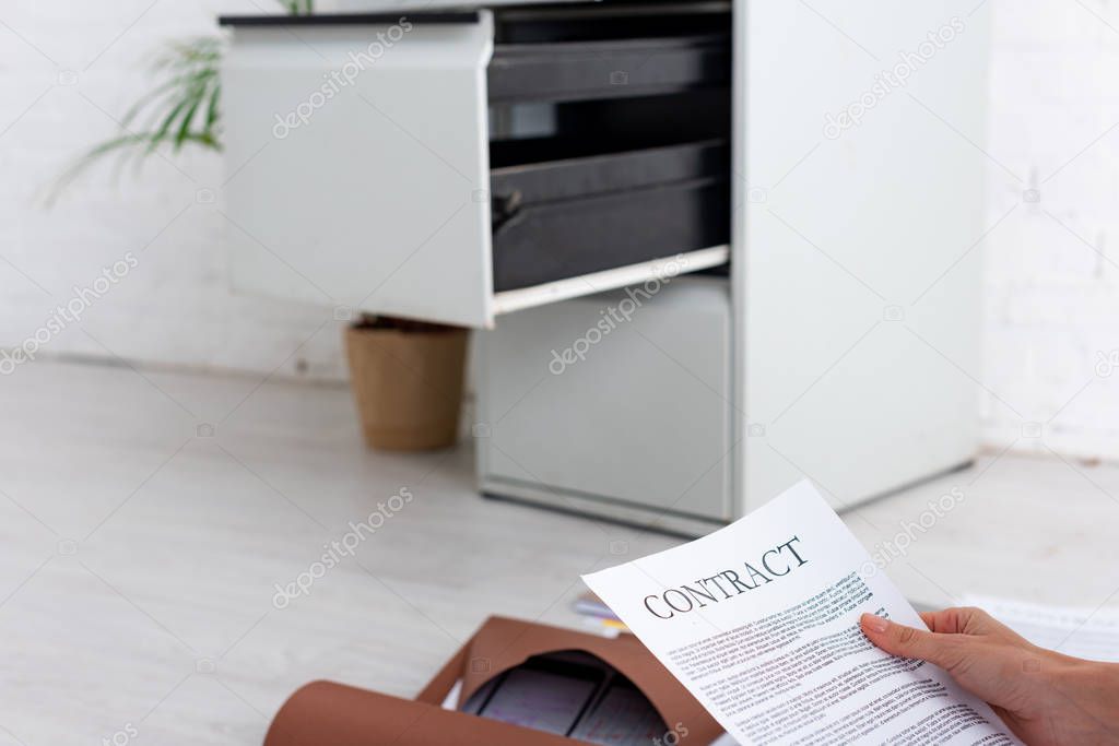 Cropped view of businesswoman holding contract near paper folders on floor