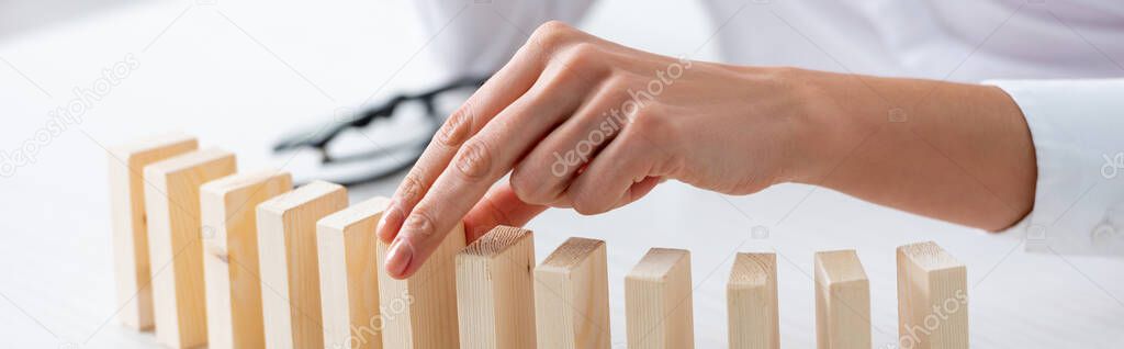 Cropped view of businesswoman holding wooden building block at table isolated on grey, panoramic shot 