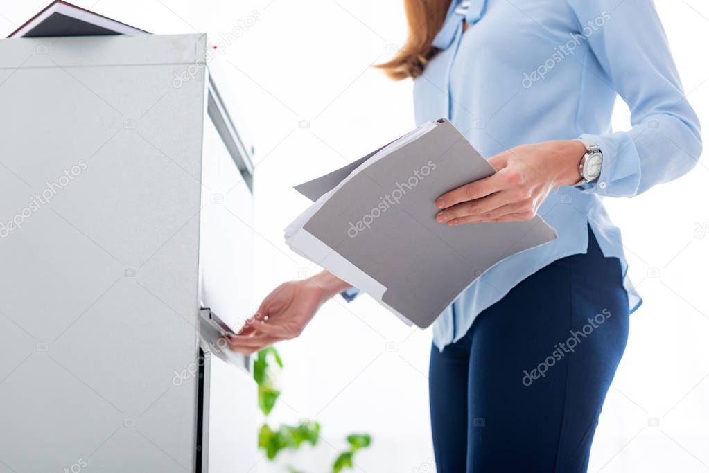 Cropped view of businesswoman holding paper folder and opening cabinet driver on white background
