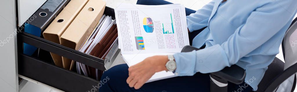 Cropped view of businesswoman holding papers with graphs near open cabinet driver with paper folders, panoramic shot 
