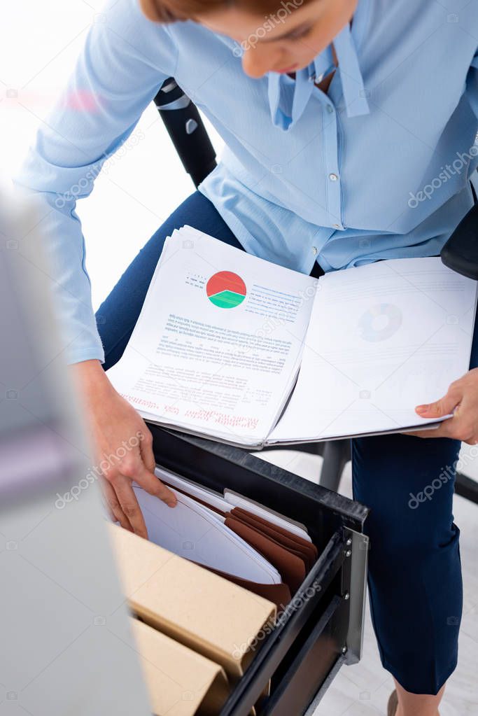 Selective focus of businesswoman holding papers with charts and searching documents in open cabinet driver isolated on white