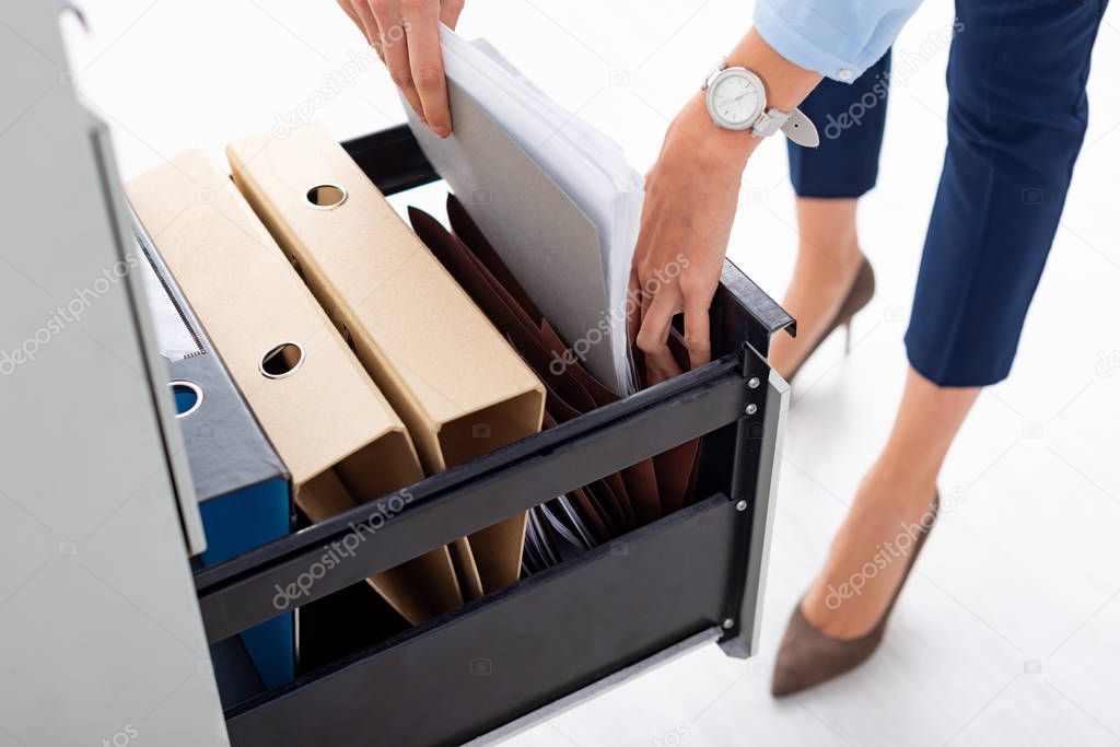 Cropped view of businesswoman taking folder with dossier from cabinet driver on white background