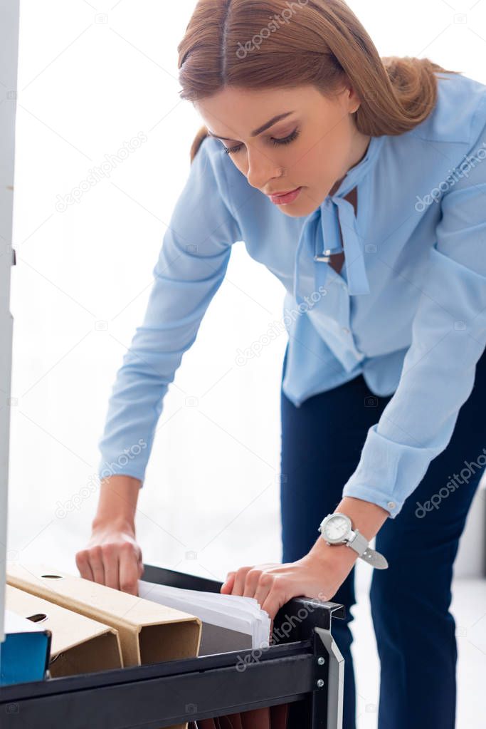 Attractive businesswoman searching folder with dossier from cabinet driver on white background