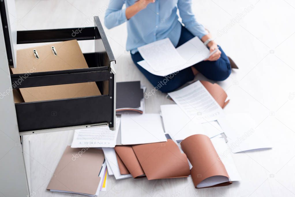 Cropped view of businesswoman with contract and documents near open cabinet driver on floor