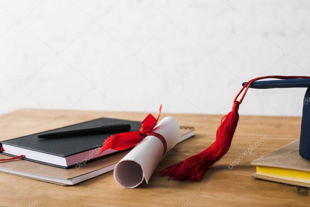 Notebooks with pen, diploma and graduation cap on table on white background