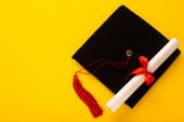 Horní pohled na černou maturitní čepici s červeným střapcem s diplomem nahoře na žlutém pozadí