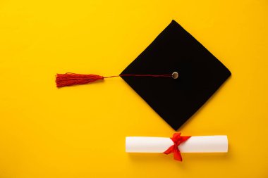 Mezuniyet şapkası ve sarı arka planda kırmızı püsküllü güzel bir diploma.