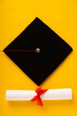 Sarı arka planda siyah mezuniyet şapkası ve güzel bir yay ile diploma manzarası.