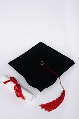 Kırmızı püsküllü siyah mezuniyet şapkası ve beyaz arka planda diploma.