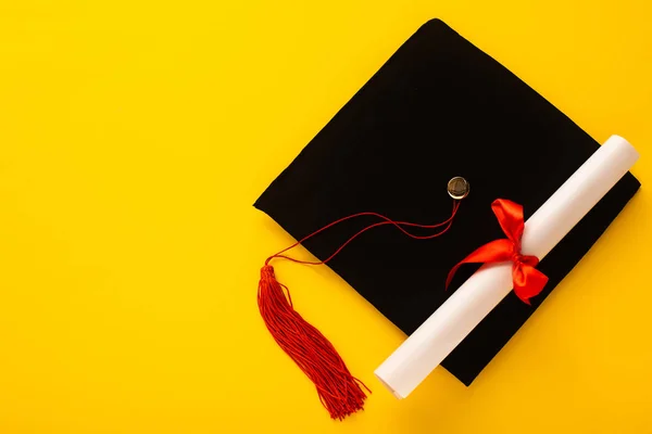 黒卒業キャップのトップビューとともに赤タッセルとともにディプロマ上の黄色の背景 — ストック写真